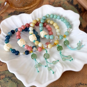 Ethnic lion-dance beaded bracelets with tassel charms and jade-like pendants in a white bowl