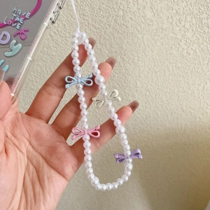 Close-up of pearl phone lanyard featuring colorful mini bow charms held in hand