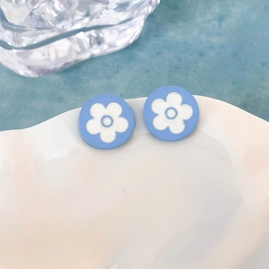 Vista macro di orecchini a lobo con fiori blu e petali bianchi su un piatto decorativo