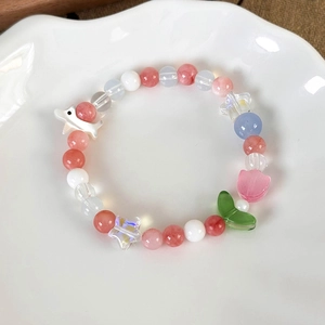 Detail of beaded bracelet with colorful ceramic shark and tulip charms on a wavy plate