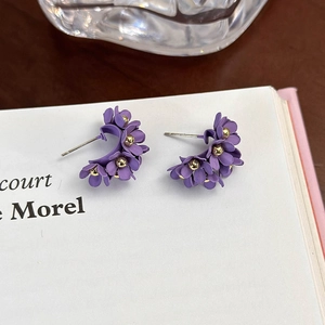 Dettaglio orecchini a fiore viola opaco con perla dorata su una pagina di libro
