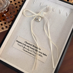 Detalle de dije de corazón plateado con lazo de cinta crema en un joyero elegante