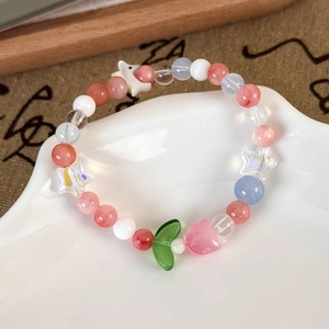 Detail shot of colorful beaded bracelet with cat and leaf charms on a white ceramic tray
