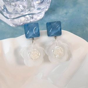 Dettaglio di orecchini quadrati blu marmorizzati con fiori in resina su piatto a conchiglia