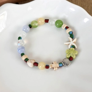 Detail of beaded marine bracelet with starfish and shell charms on a white plate