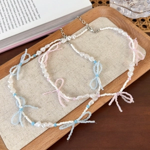 Pastel beaded bow necklace with faux pearls and blue crystal accents on a tray