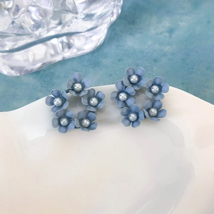 Dettaglio di orecchini a lobo con fiori blu opaco e perle su un vassoio di ceramica bianca