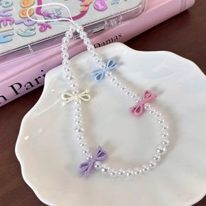 Detail of sweet pearl phone charm featuring colorful bows on an elegant shell tray