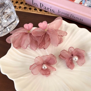 Détail de boucles d'oreilles florales roses et pinces à perles sur plateau coquillage