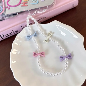 Detailed view of pearl phone strap with colorful pastel bow accents on a white plate
