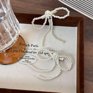 Elegant white pearl bow hair clips in French style on a brown jewelry tray for women