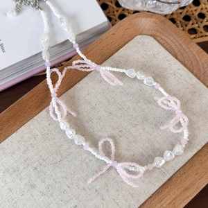Detailed macro view of beaded pearl necklace with pink crystal bows on a rustic tray