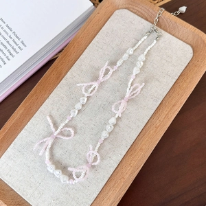 Detail of pink beaded bow necklace with white heart charms on a rustic wooden tray