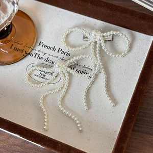 Detailed macro view of white pearl bow hair clips with elegant cascading fringe tassels
