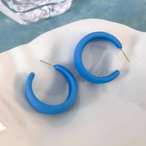 Dettaglio di orecchini a C blu opaco con trama fine su un vassoio bianco elegante