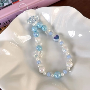 Close-up of blue and white beaded phone strap with heart and star charms on ceramic plate
