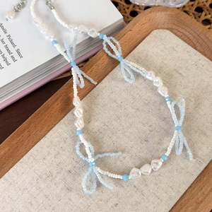 Detailed close-up of beaded choker with light blue bows and pearls on a wooden tray