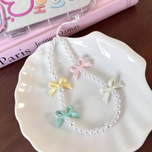 Detail of sweet pearl phone charm with colorful resin bows on white shell plate
