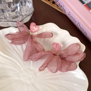 Détail de la boucle d'oreille cœur rose avec nœud en mousseline sur plateau coquille