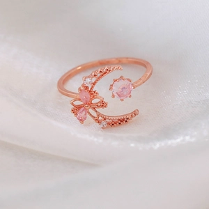 Detail of rose gold moon ring with pink crystals and butterfly design on silk background