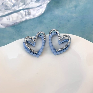 Dettaglio di orecchini a cuore blu con strass bianchi su un piatto di ceramica bianca