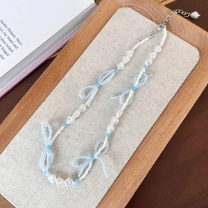 Detailed macro view of blue beaded bow necklace with white pearls and metal lobster clasp