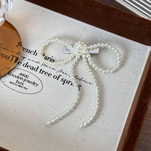 Elegant white pearl bow hair clip with silver metal base shown on vintage display tray