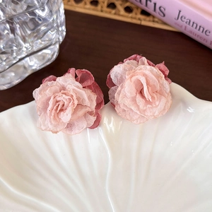 Gros plan de boucles d'oreilles fleurs en tissu rose sur un plateau en forme de coquillage