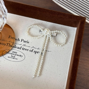 Detailed macro view of an elegant white faux pearl woven bow hair clip with silver metal base