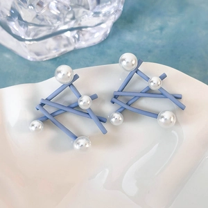 Dettaglio di orecchini geometrici blu opaco con perle finte su un piatto di ceramica bianca