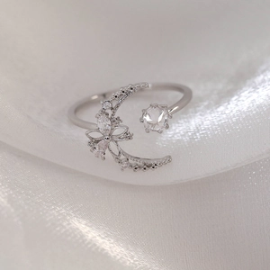Macro shot of silver ring with zircon moon and flower design on white silk background
