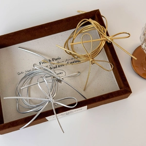 Minimalist Y2K style silver and gold bow hair ties on vintage linen background