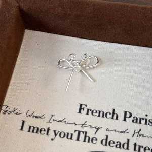 Gros plan sur un ear cuff nœud argenté présenté sur une carte d'exposition beige