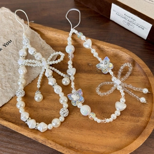 Elegant pearl phone charm strap with white bow and heart beads on a vintage wooden tray