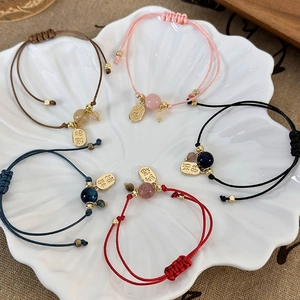 Detail of colorful woven bracelets with lucky charm tags and gemstone beads on a white tray