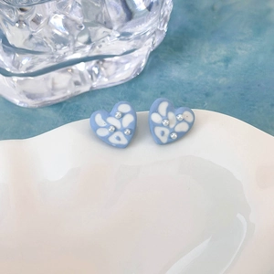 Dettaglio di orecchini a cuore blu con pois bianchi e piccole perle su un vassoio bianco