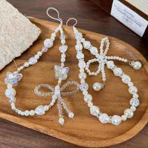 Elegant beaded phone strap with pearls and bowknot on a vintage wooden tray