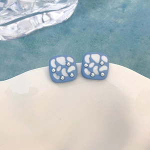 Dettaglio di orecchini a lobo quadrati azzurri con perline argento su bordo ceramico