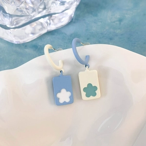 Dettaglio di orecchini floreali blu e bianchi su un piatto di ceramica bianca