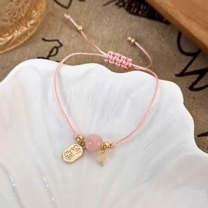 Macro shot of pink braided cord bracelet with gold charm and carved hibiscus stone