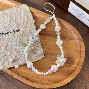 Detail shot of pearl phone wrist strap with aurora beads and bow knot in a wooden tray
