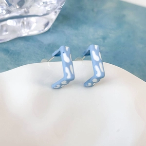 Dettaglio di orecchini a perno quadrati azzurri con stampa mucca su vassoio ceramica