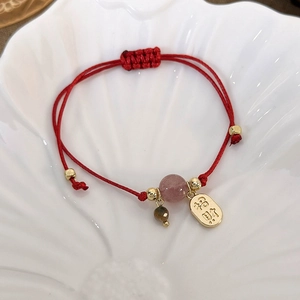 Detailed close-up of woven red cord bracelet with a gold luck charm and crystal bead