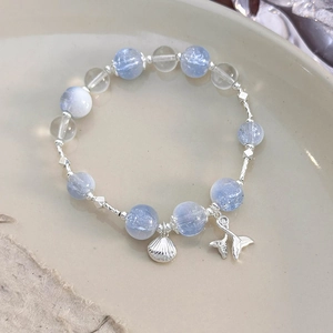 Close-up of shell and mermaid tail silver charms on a light blue beaded bracelet