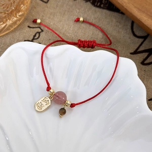 Detailed shot of red woven bracelet with Nafu gold pendant and pink strawberry quartz