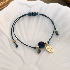 Detailed close-up of blue braided rope bracelet with golden Fu charm and adjustable knot