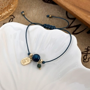 Macro detail of hand-woven blue cord bracelet with gold lucky charm and blue gemstone