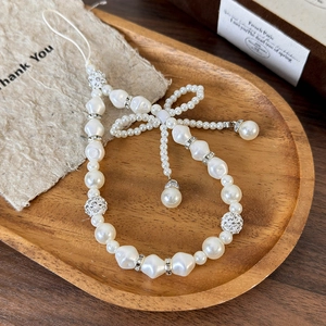 Detail of elegant white pearl phone strap with beaded bow on a wooden tray