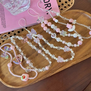 Detailed view of four pink beaded phone charms with bows and flowers on a wooden tray