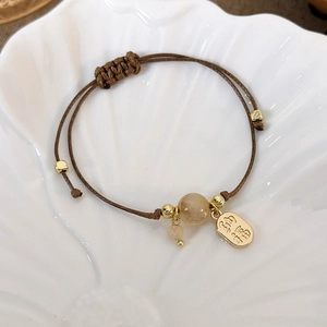 Macro shot of brown braided rope bracelet with golden Fu charm and mineral bead detail